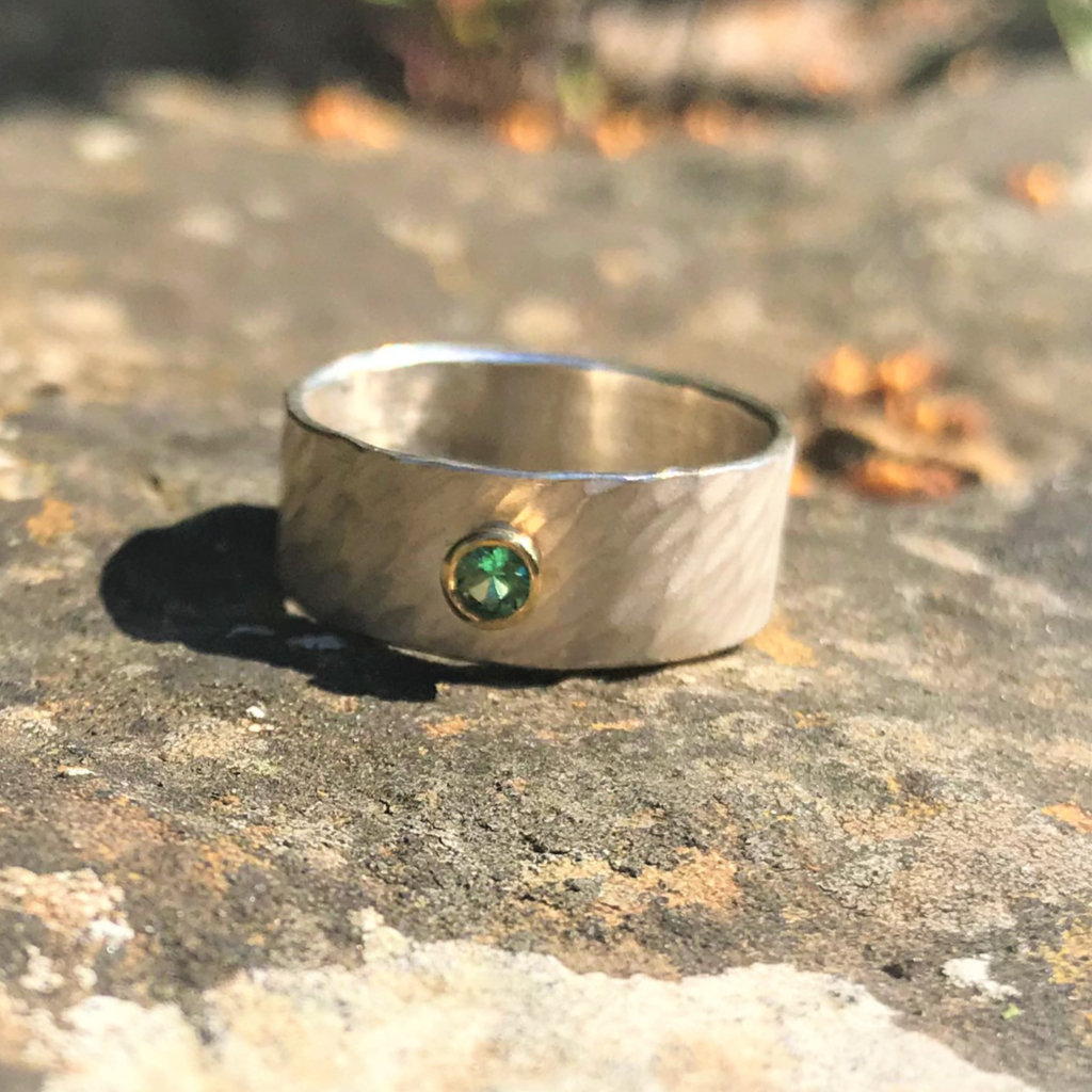 Faceted emerald in yellow gold setting on wide rays silver band