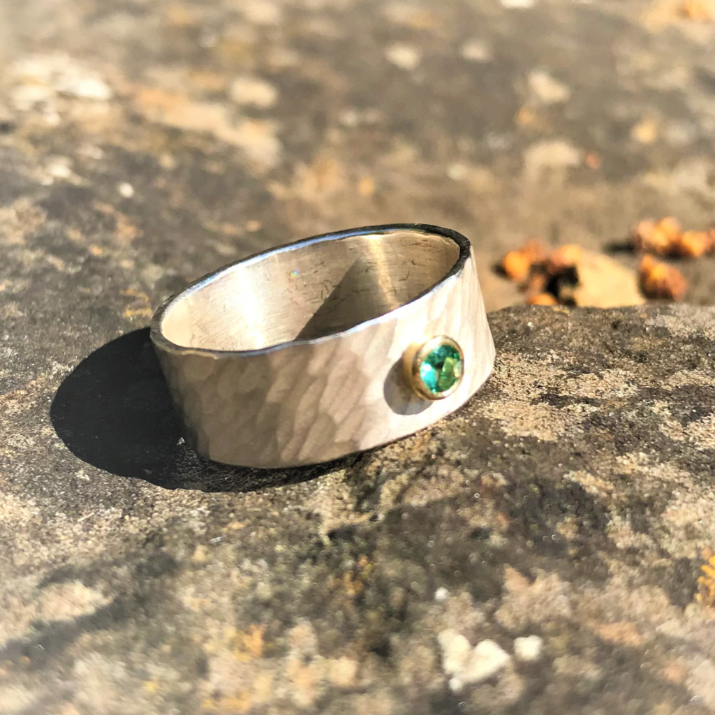 Faceted emerald in yellow gold setting on wide rays silver band