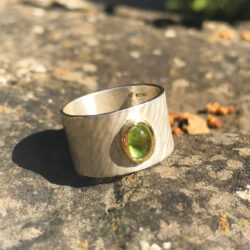 Oval cabochon peridot in yellow gold setting on wide rays silver band