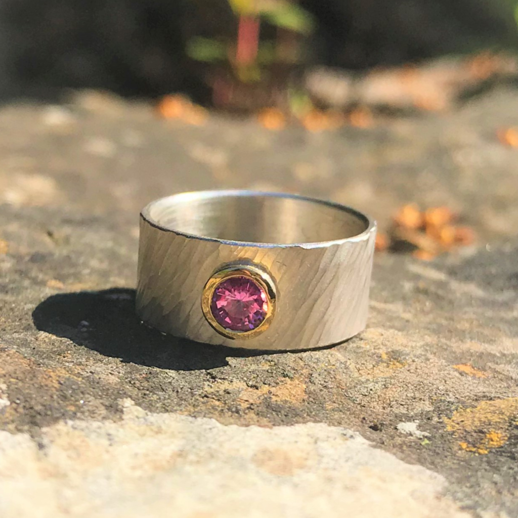Pink sapphire in gold setting on wide rays silver band