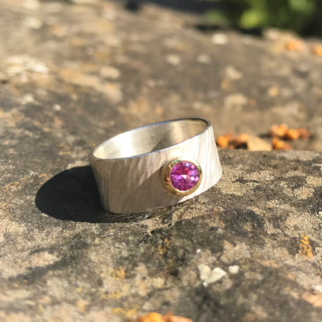 Pink sapphire in gold setting on wide rays silver band