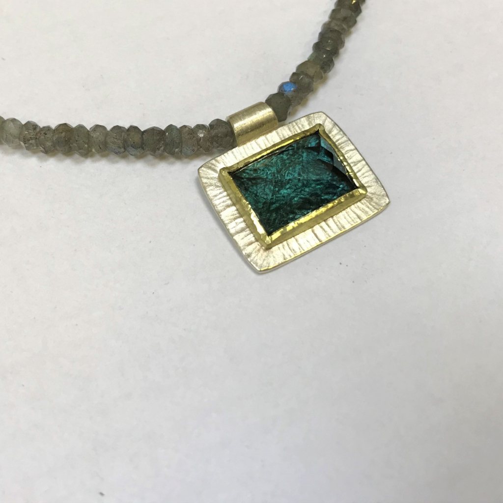 Blue tourmaline cushion set in gold on a necklace of labradorite with silver clasp