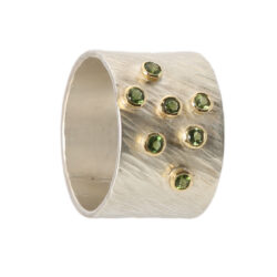Seven green tourmalines each set in gold on a wide rays silver band