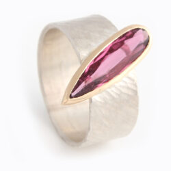 Pink tourmaline tear drop in red gold setting on broad silver rays textured band